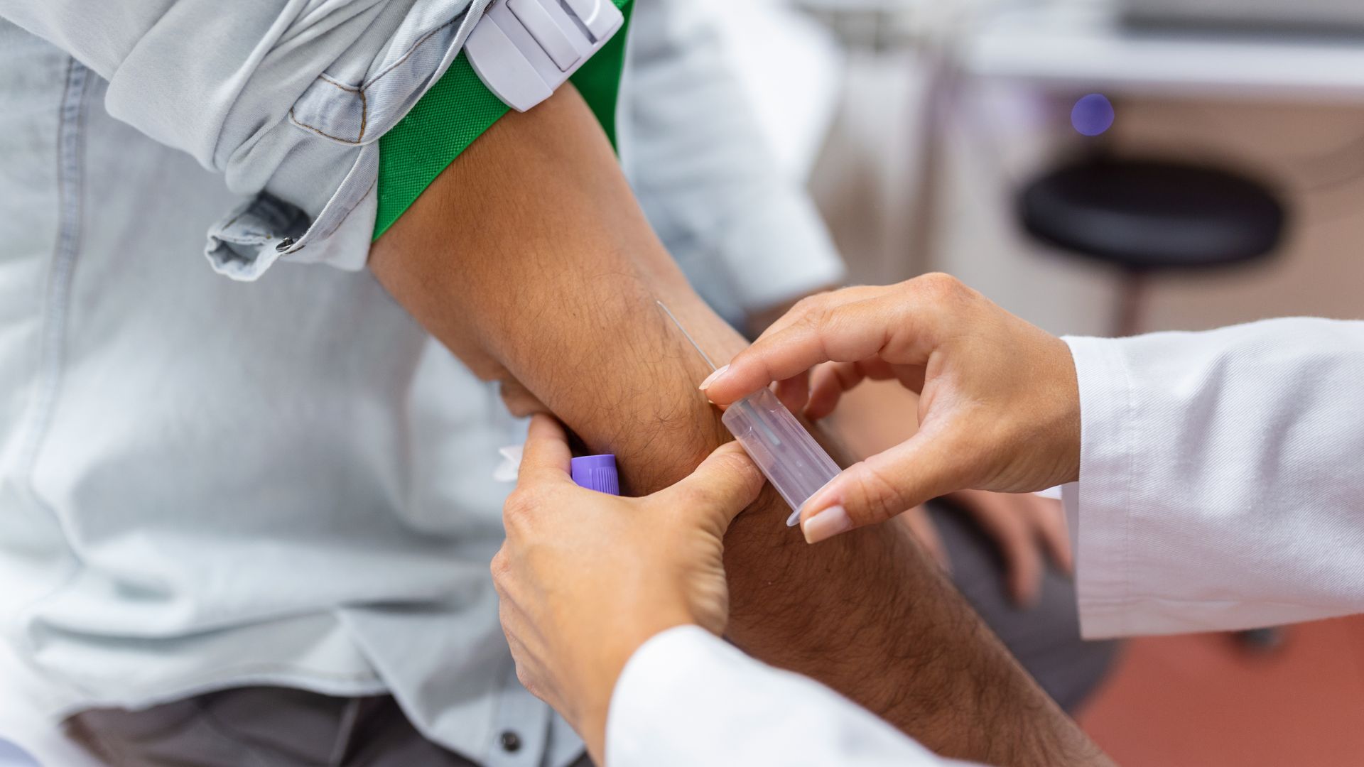 Skilled focused young phlebotomy technician applying a tourniquet to a male patient arm for venipuncture